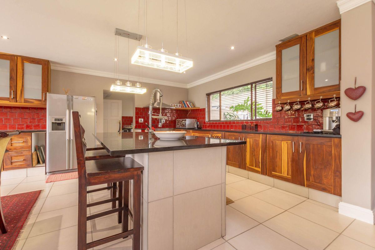 A functional kitchen featuring wooden cabinetry, granite countertops, a central island with breakfast bar seating, and a striking red tiled backsplash.