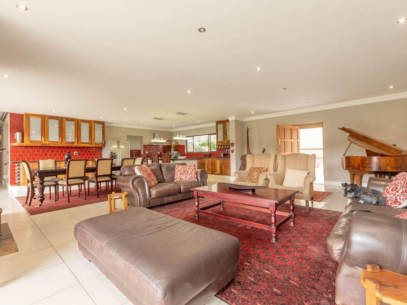 Spacious open-plan living and dining area featuring tiled flooring, recessed lighting, and a kitchen with red tiled splashbacks and wooden cabinetry.
