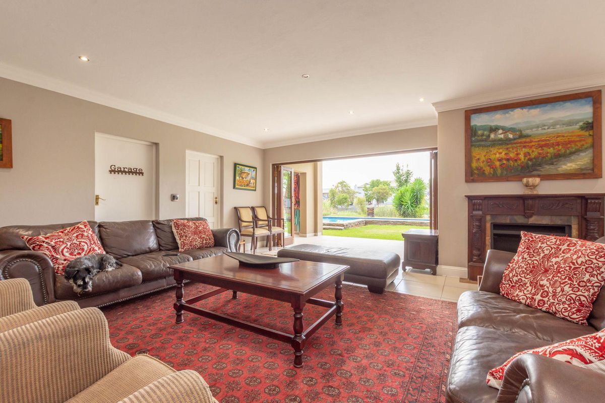 Spacious living room featuring a traditional fireplace, recessed lighting, and large folding doors that open onto a patio with garden and pool views.