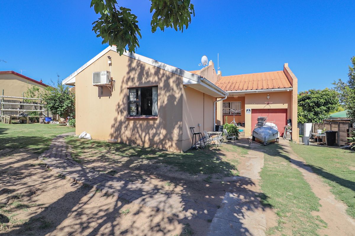 Rear view of the house featuring a single garage, paved driveway, and exterior air conditioning unit set within a spacious garden area.