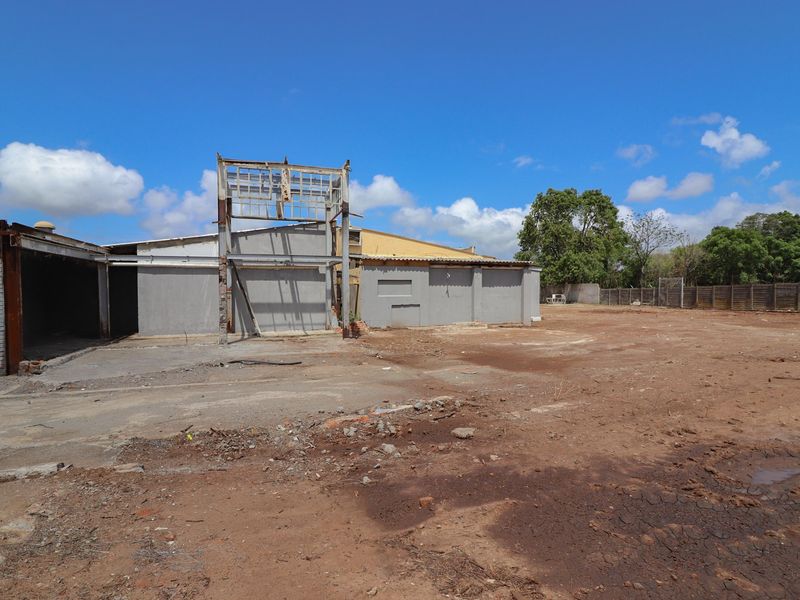 A commercial property exterior featuring a large open yard area and a partially demolished or unfinished building structure with exposed steel framing.