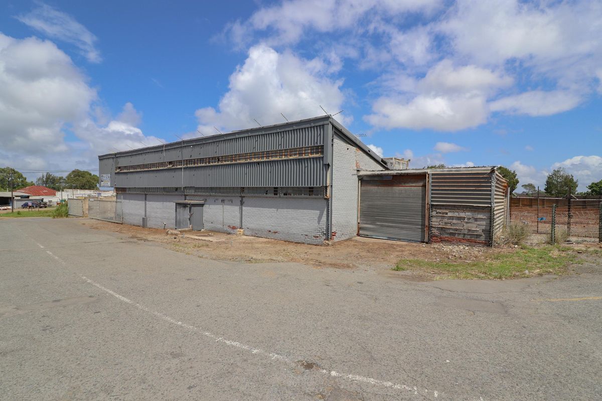 Exterior view of a commercial warehouse building featuring metal cladding, roller shutter doors, and perimeter security fencing.