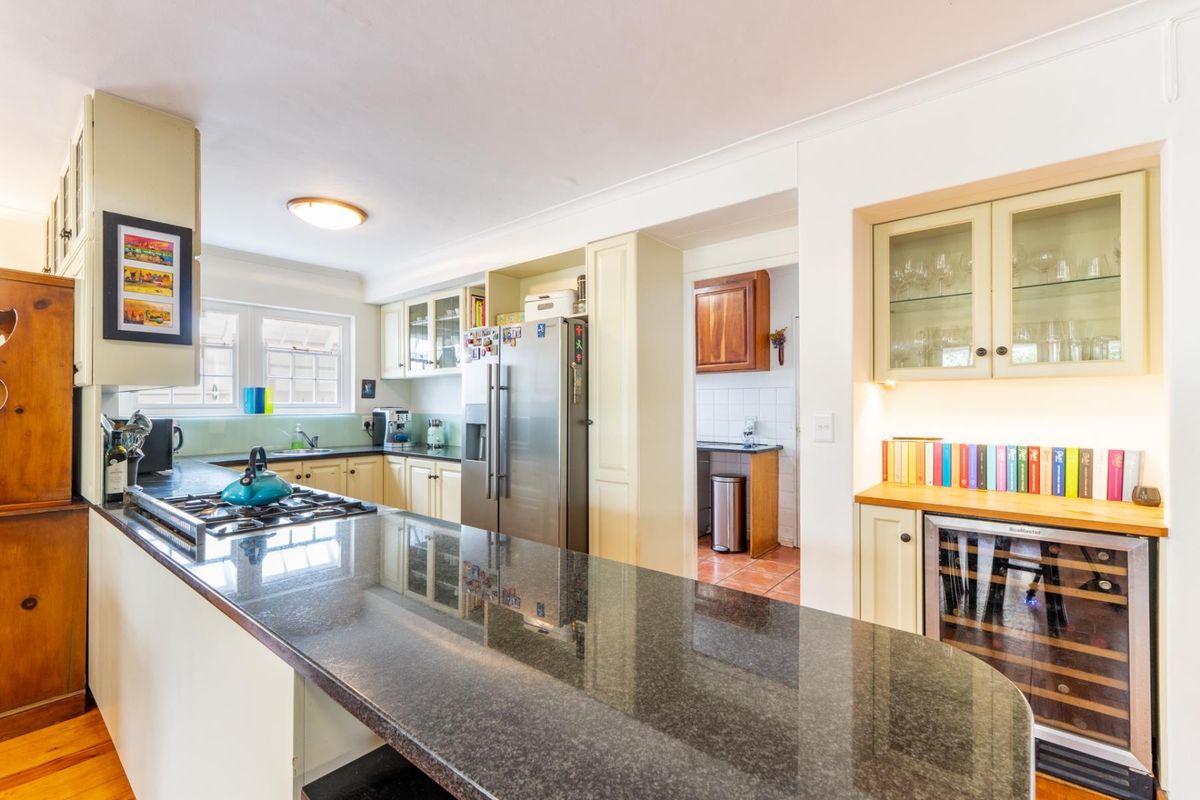 A well-appointed kitchen featuring granite countertops, a gas hob, integrated wine cooler, and ample cabinetry with glass-fronted display units and under-cabinet lighting.