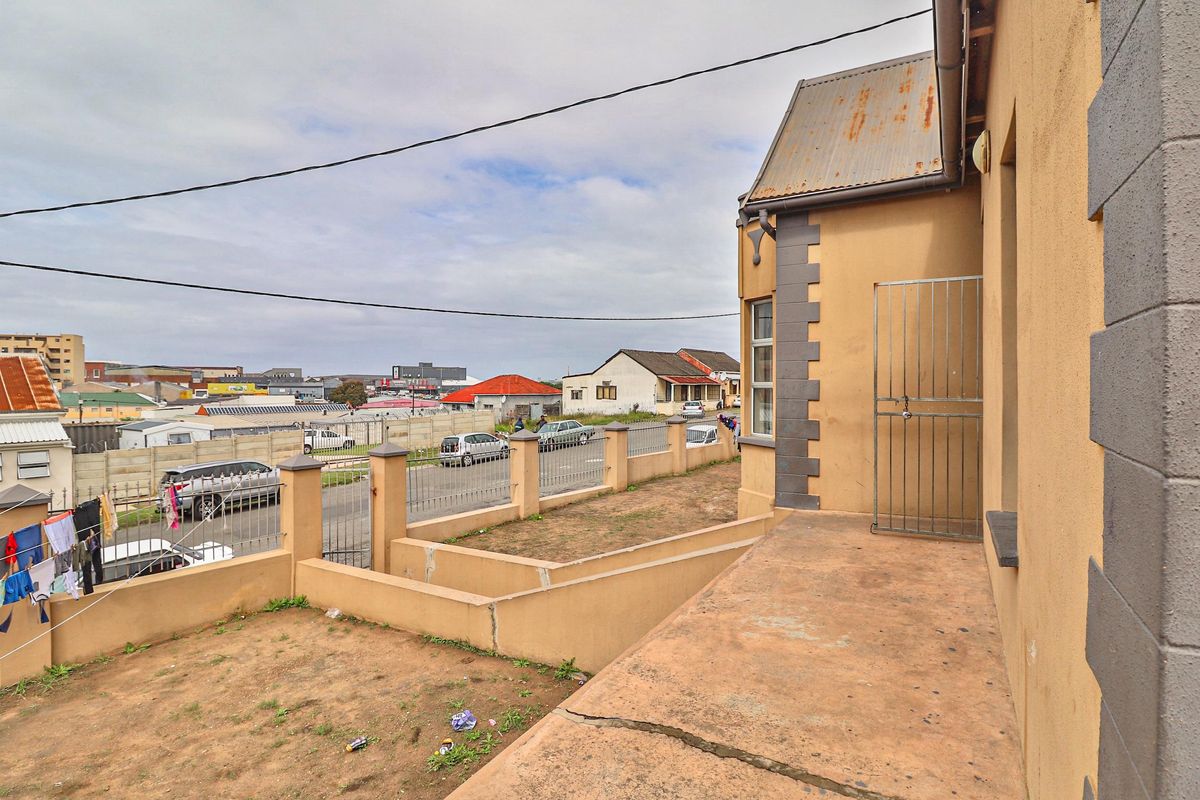 Exterior view of the property featuring a concrete patio area, perimeter wall with metal fencing, and a corrugated iron roof.