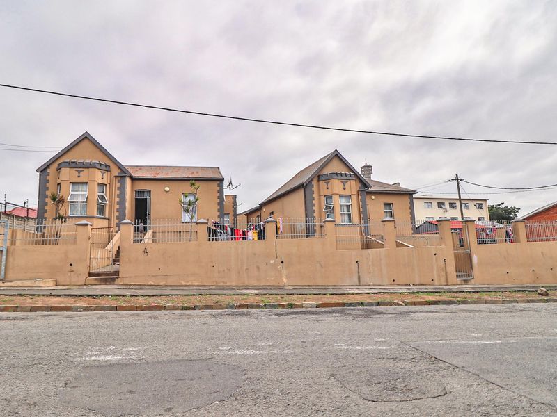 Street view of a residential property featuring two symmetrical dwelling structures behind a solid boundary wall with metal fencing.