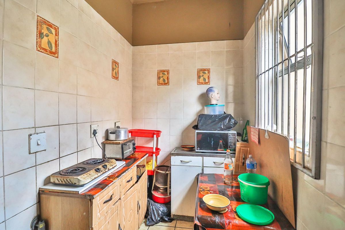 A compact kitchen featuring tiled walls, built-in cabinetry, and a window with security bars, requiring cosmetic updates to modernize the space.