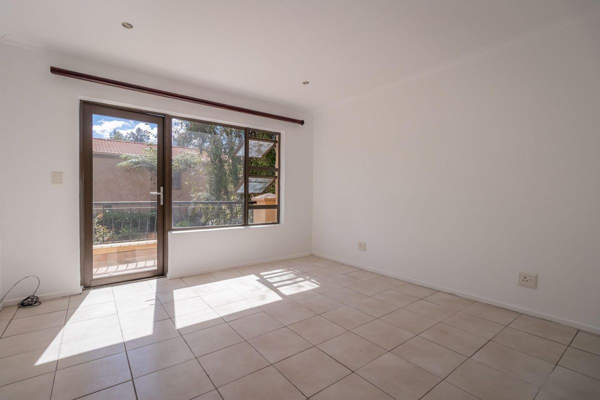 A bright, empty bedroom featuring neutral floor tiles, recessed lighting, and a glass door providing access to an outdoor balcony area.
