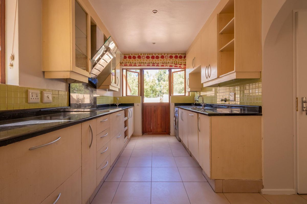 A functional galley-style kitchen featuring dark stone countertops, light-toned cabinetry, tiled flooring, and direct access to the rear garden.