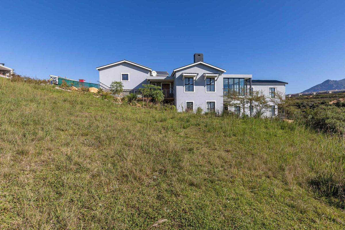 A view of the rear elevation of a modern residential property set on a sloped, grassy plot with mountain views.