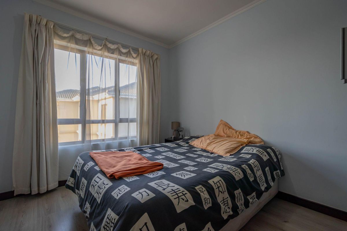 A bedroom featuring light-toned laminate flooring, a large window with natural light, and crown molding.