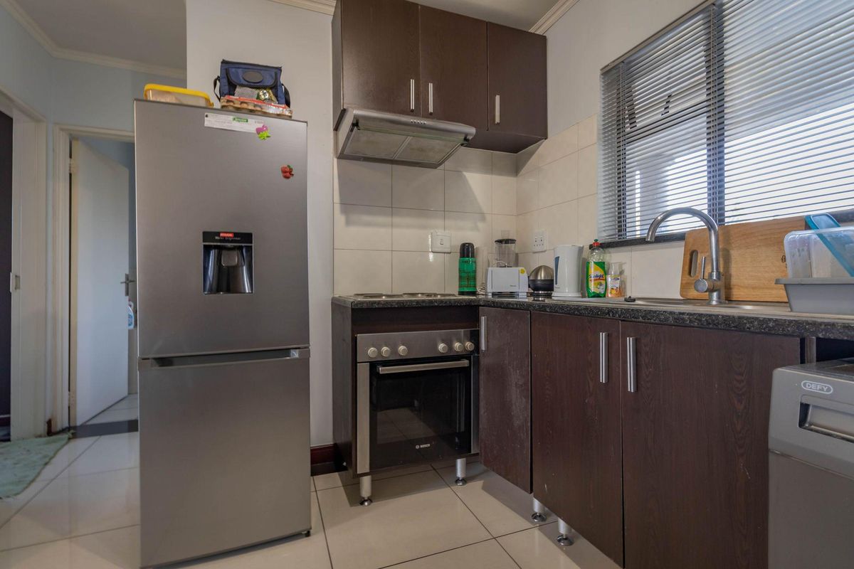 Compact kitchen featuring dark wood cabinetry, granite-look countertops, built-in oven with extractor fan, and tiled flooring.