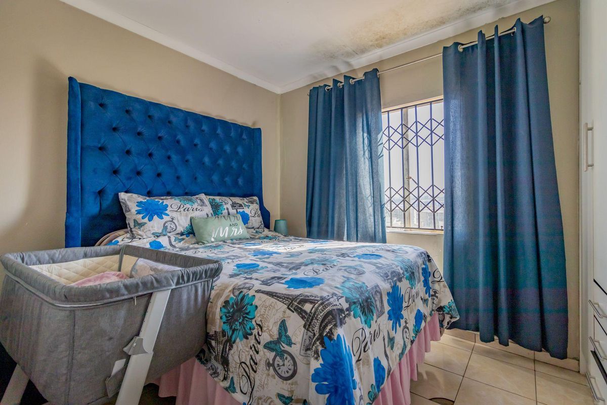 A bedroom featuring tiled flooring and a window fitted with security bars, showing visible signs of water damage on the ceiling.