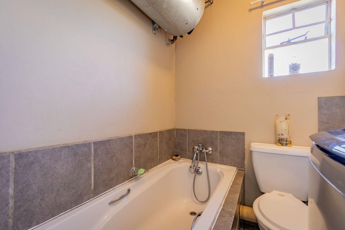 A functional bathroom featuring a bathtub with a handheld shower mixer, a standard toilet, and an exposed wall-mounted water heater.