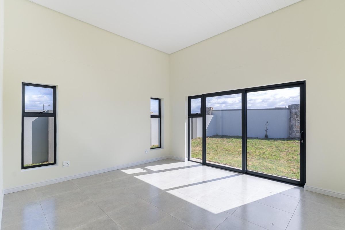 A bright, empty living room featuring large black-framed sliding glass doors that open onto a private rear garden.