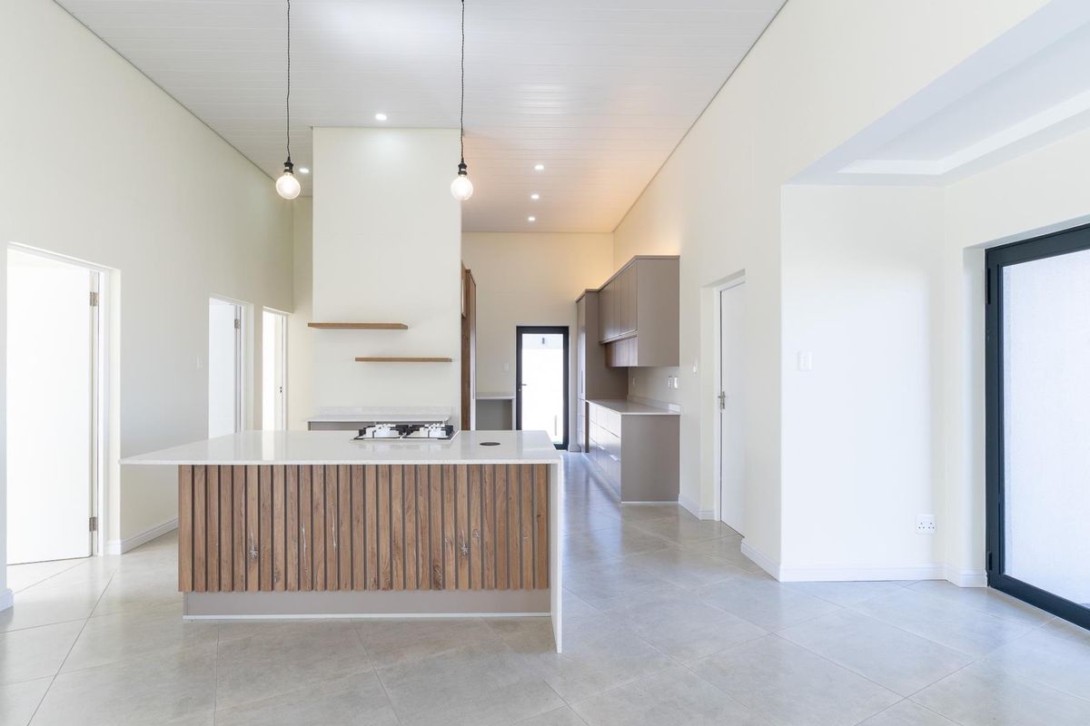 Modern open-plan kitchen featuring a central island with a built-in gas hob, sleek cabinetry, and neutral tiled flooring in a bright, contemporary space.