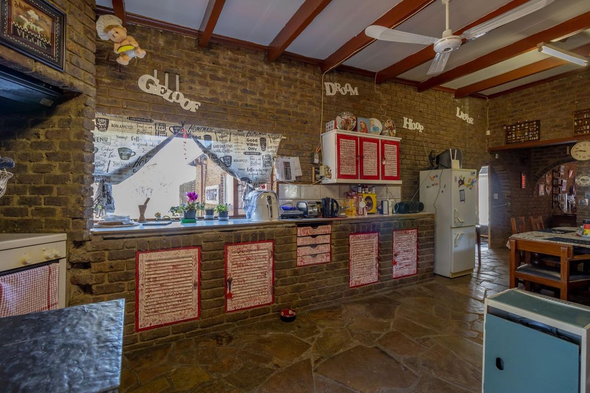 Rustic kitchen featuring exposed brick walls, timber ceiling beams, stone flooring, and custom built-in brick cabinetry with integrated storage.