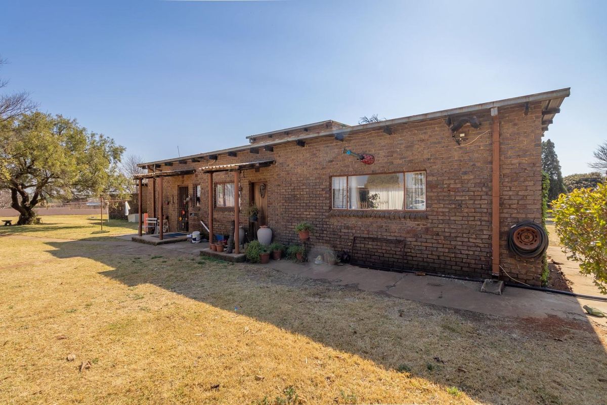 Rear view of a single-story brick house featuring a covered patio area, established garden, and exposed brick facade.