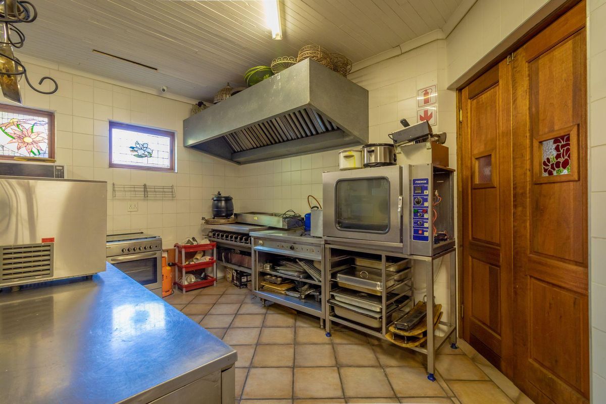 Commercial kitchen featuring stainless steel work surfaces, industrial oven, gas hob, and a large extractor hood with tiled walls and flooring.