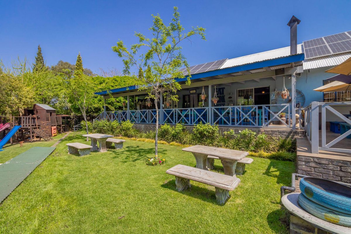 A rear view of the commercial property featuring a covered patio deck, landscaped garden area, and solar panel installation on the roof.