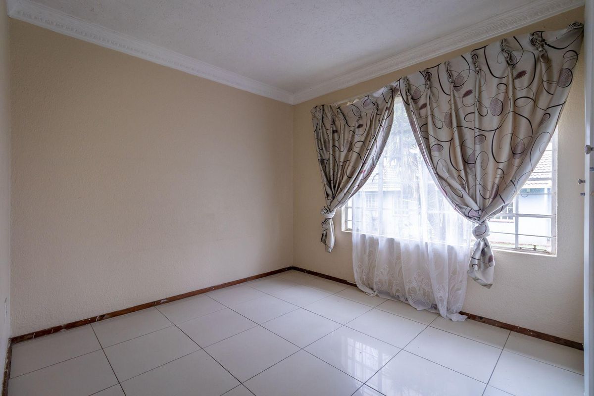 A bright, empty bedroom featuring neutral tiled flooring, decorative ceiling cornicing, and a large window with natural light.