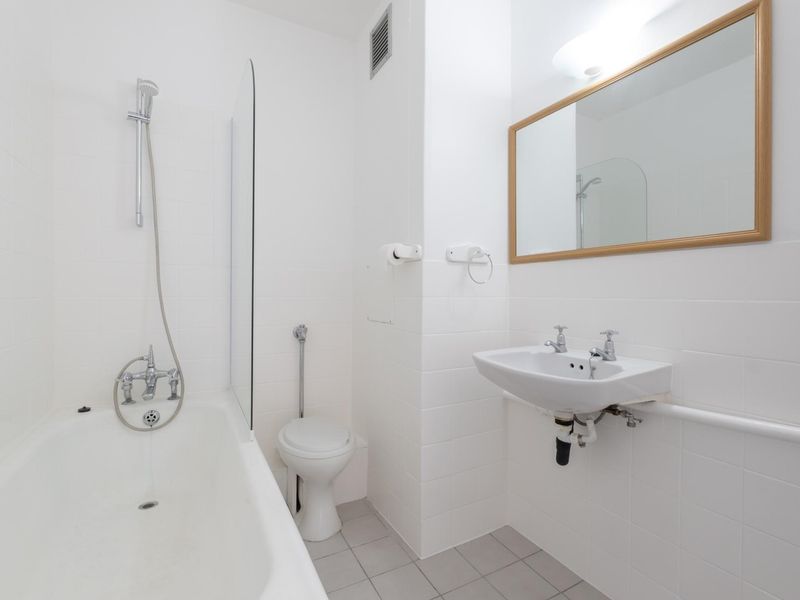 A clean, functional bathroom featuring a white bathtub with shower mixer, wall-mounted basin, and neutral tiled finishes throughout.