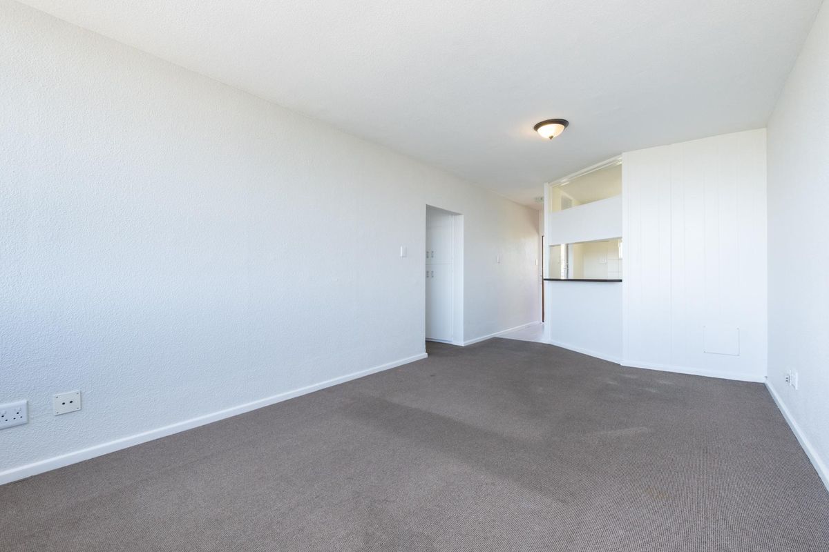 An empty living room featuring neutral carpet flooring and a convenient pass-through window connecting to the kitchen area.