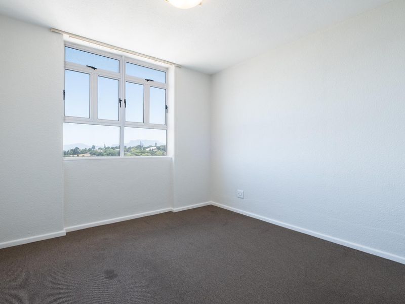 A bright, empty bedroom featuring neutral walls, carpeted flooring, and a large window with natural light and scenic views.