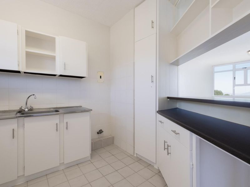 A clean and functional scullery featuring white built-in cabinetry, a stainless steel sink, and tiled finishes, offering practical utility space.