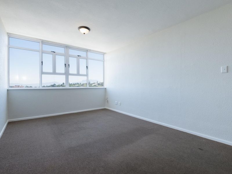A bright, empty bedroom featuring large windows with natural light, neutral walls, and carpeted flooring, offering a blank canvas for personalization.
