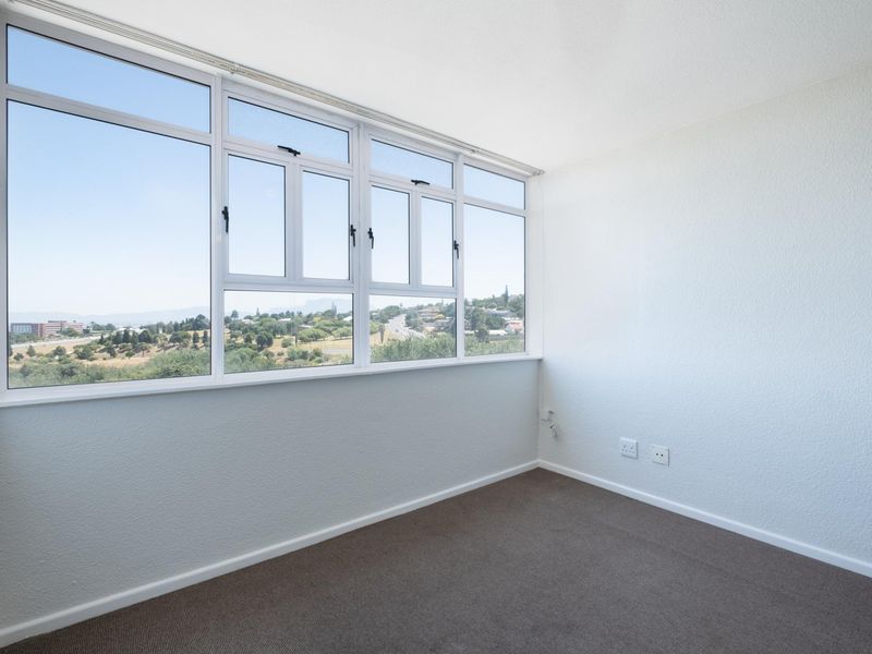 A bright, empty bedroom featuring large windows with expansive views, neutral wall finishes, and carpeted flooring.