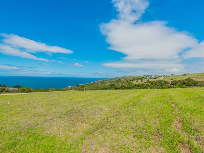 A scenic view of a vacant residential plot featuring expansive green grassland with a clear outlook over the coastline and ocean.
