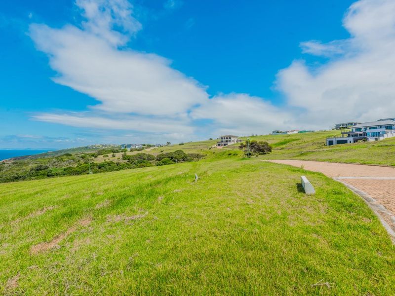 A vacant residential plot featuring a paved driveway and expansive coastal views in a developed estate setting.