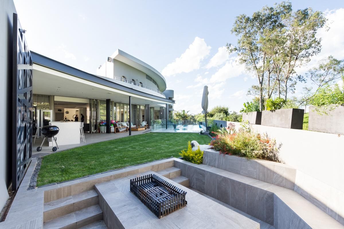 Spacious rear garden featuring a sunken fire pit area, manicured lawn, swimming pool, and a covered patio seamlessly connected to the main living space.