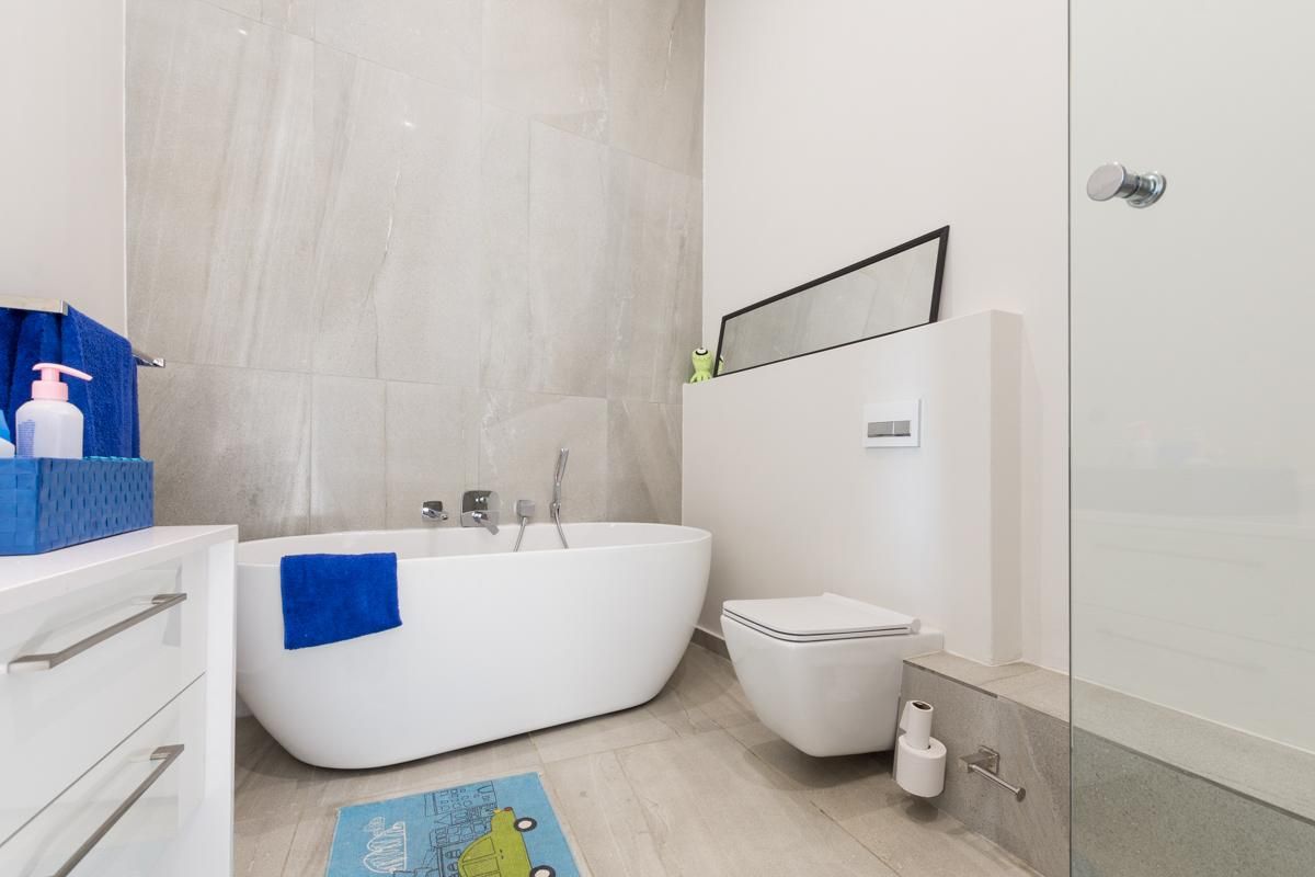 Modern bathroom featuring a freestanding bathtub, wall-mounted toilet, and large format neutral floor and wall tiles.