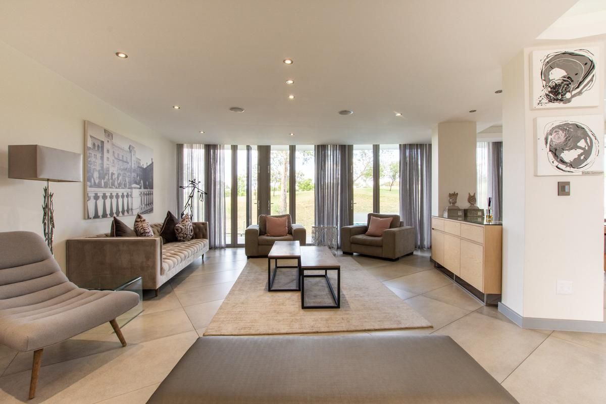 Spacious living room featuring large floor-to-ceiling windows, recessed ceiling lighting, and neutral tiled flooring, offering a bright and modern atmosphere.