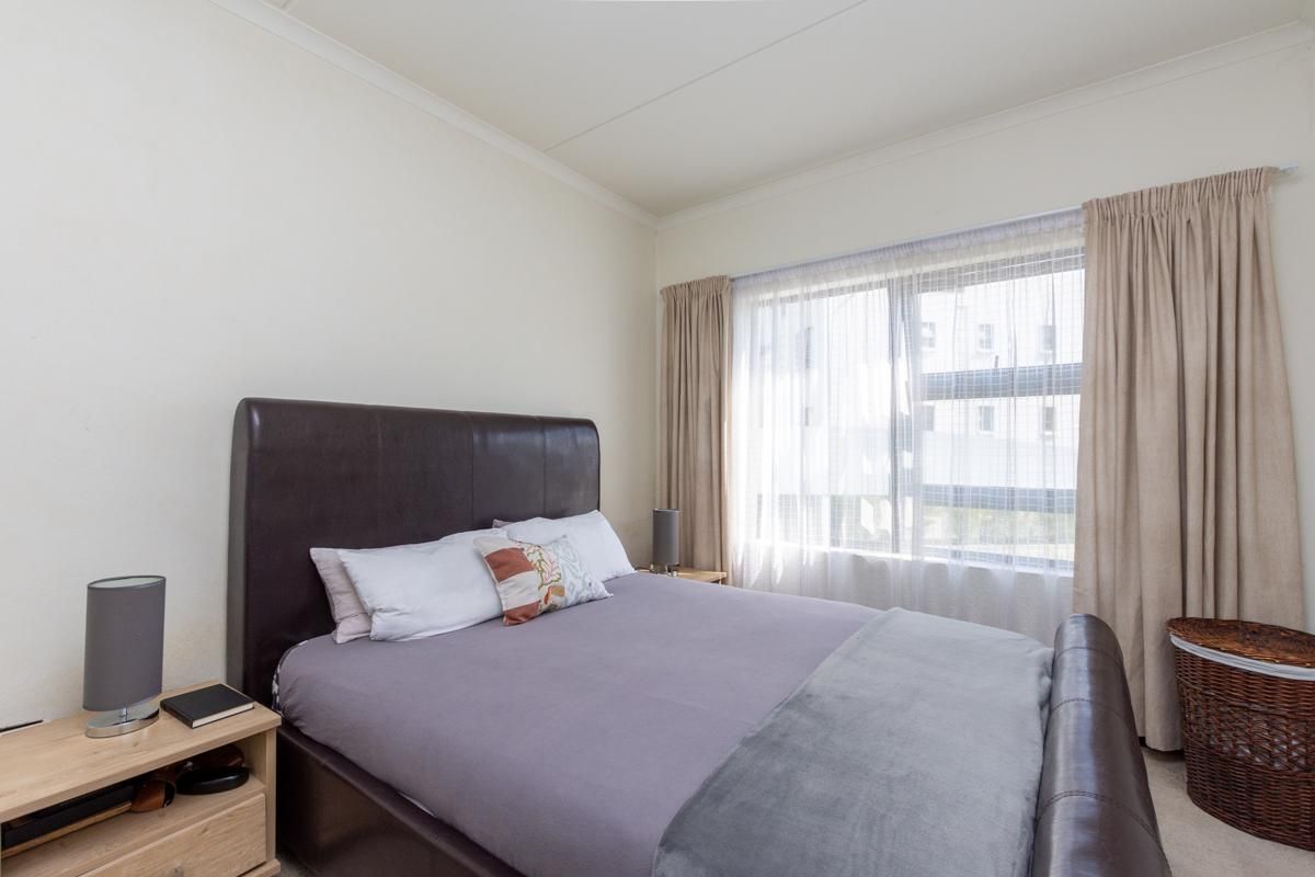 A well-lit bedroom featuring neutral walls, carpeted flooring, and a large window with curtain tracks.