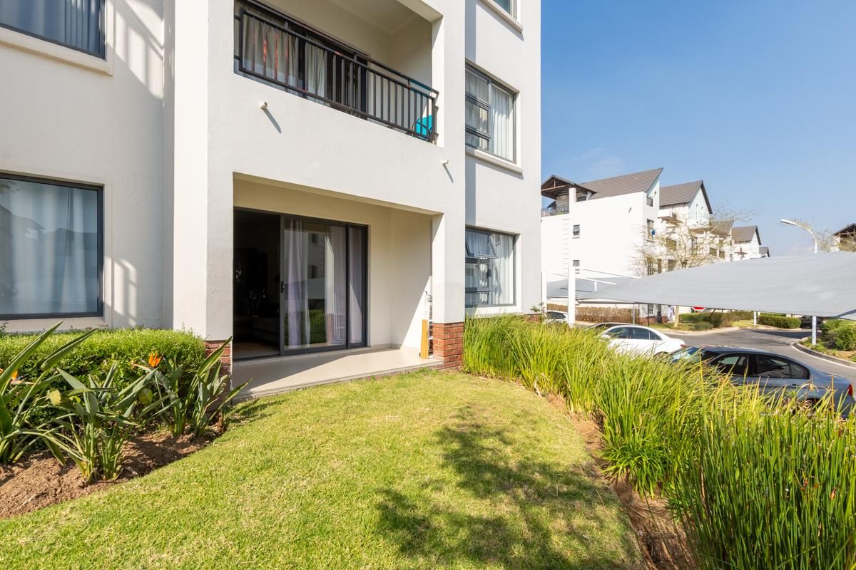 Ground floor apartment exterior featuring a private patio area, landscaped garden, and modern building facade with sliding glass doors.