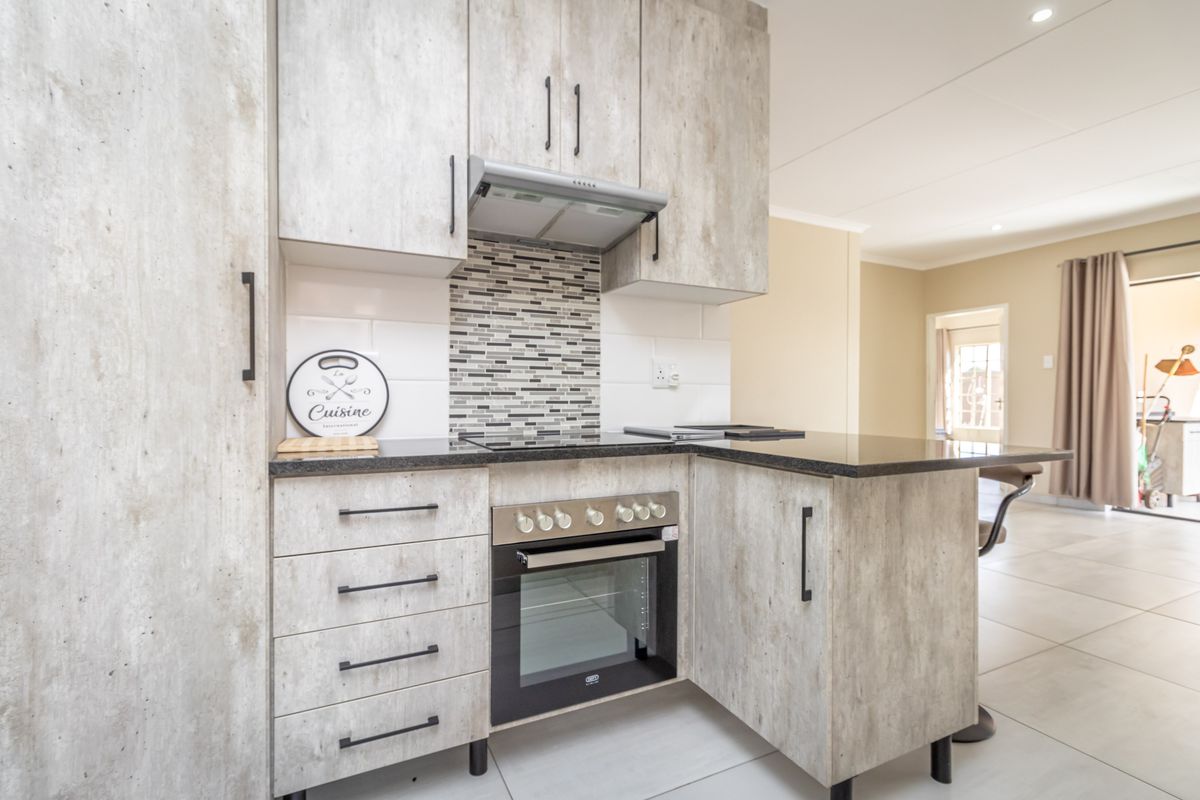 Modern kitchen featuring light wood-grain cabinetry, granite countertops, a built-in oven, glass cooktop, and a mosaic tile backsplash.