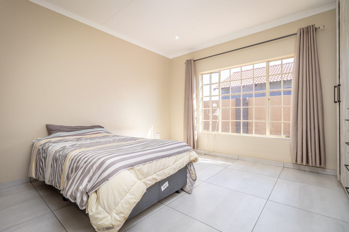A bright bedroom featuring large grid-pane windows, neutral tiled flooring, and built-in wardrobe cabinetry.