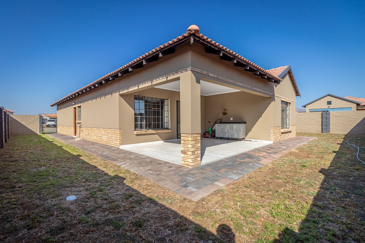 A well-maintained rear exterior view featuring a covered patio with tiled flooring, brick accents, and a surrounding paved walkway in the garden.