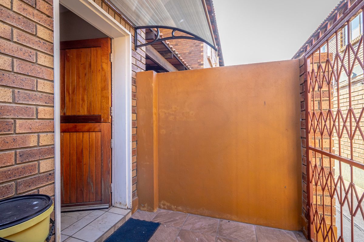 A private exterior courtyard area featuring tiled flooring, a solid wood door, and a protective metal security gate.