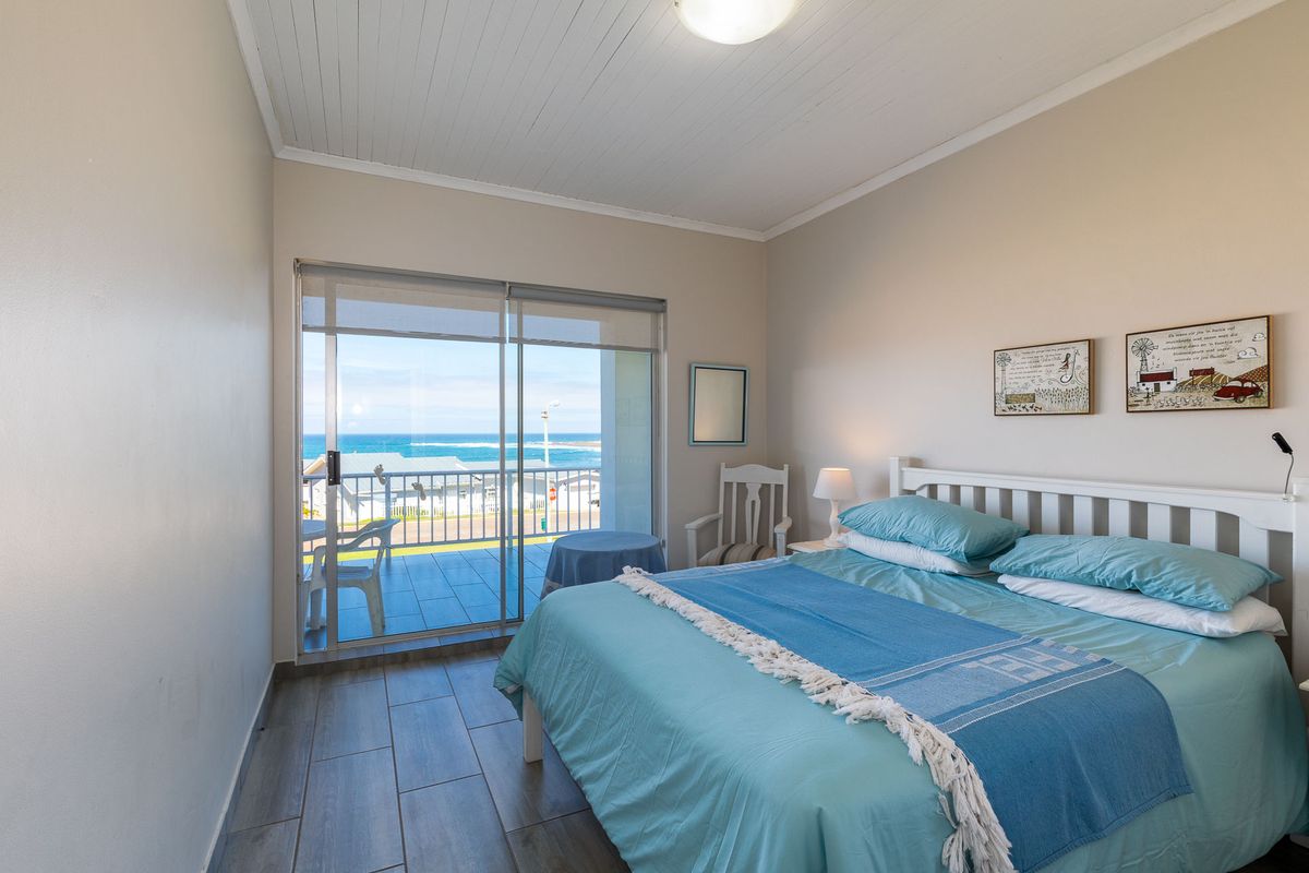A bedroom featuring tiled flooring, a white timber-paneled ceiling, and sliding glass doors that open onto a balcony with ocean views.