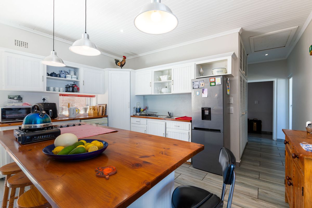 A bright kitchen featuring white cabinetry, a wooden island countertop, pendant lighting, and tiled flooring, offering a functional and inviting culinary space.