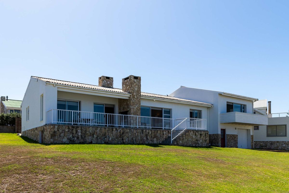 Rear view of the house featuring a stone-clad base, elevated patio with white railings, and two prominent stone chimneys.