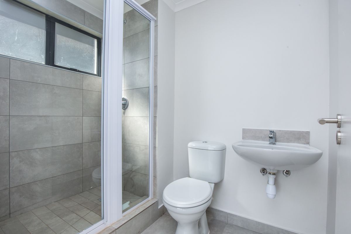A modern bathroom featuring a glass-enclosed shower with grey tiling, a wall-mounted basin, and a standard toilet.