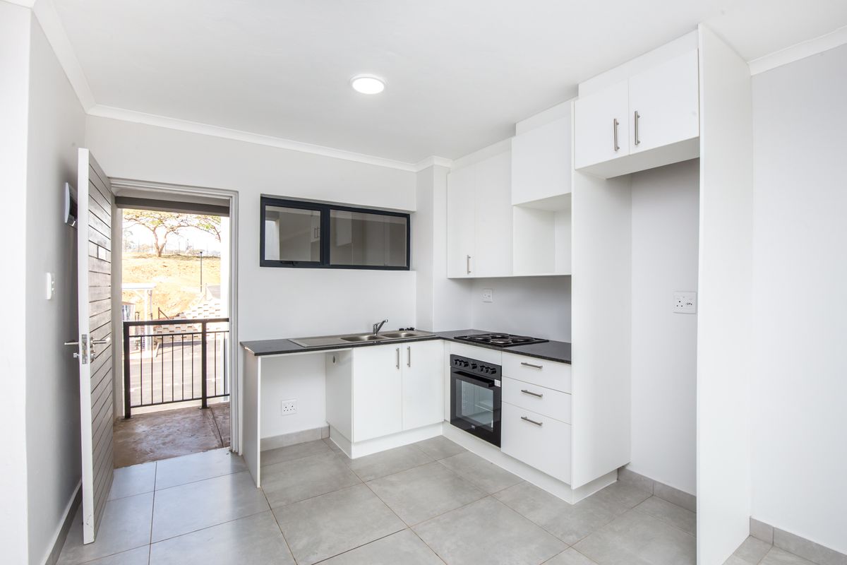 Modern kitchen featuring white cabinetry, dark countertops, built-in oven and hob, and tiled flooring with direct access to an outdoor balcony area.