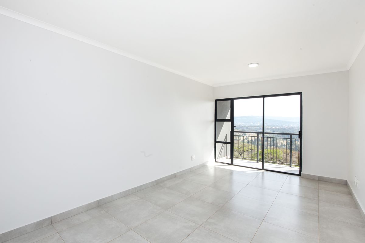 A bright, empty bedroom featuring neutral floor tiles and a large sliding glass door leading to a balcony with scenic views.