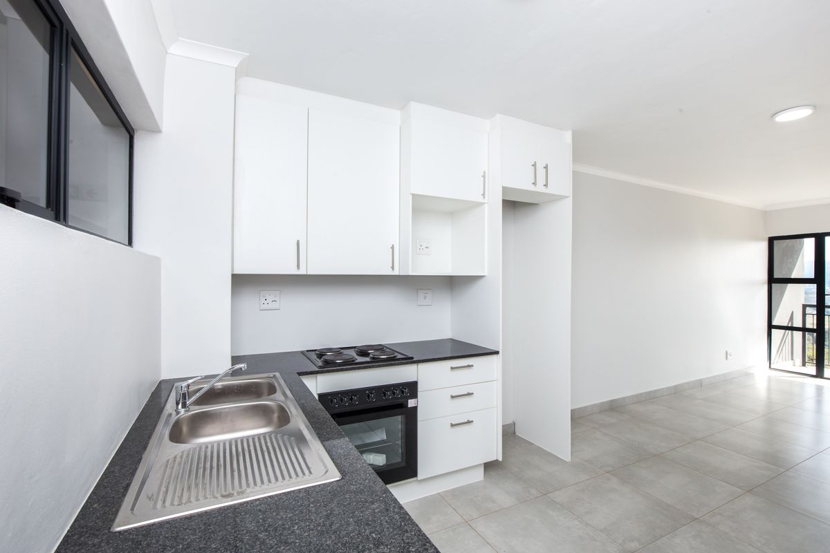 Modern open-plan kitchen featuring white cabinetry, dark granite countertops, a built-in oven, and a stainless steel double sink, flowing into a bright living area.
