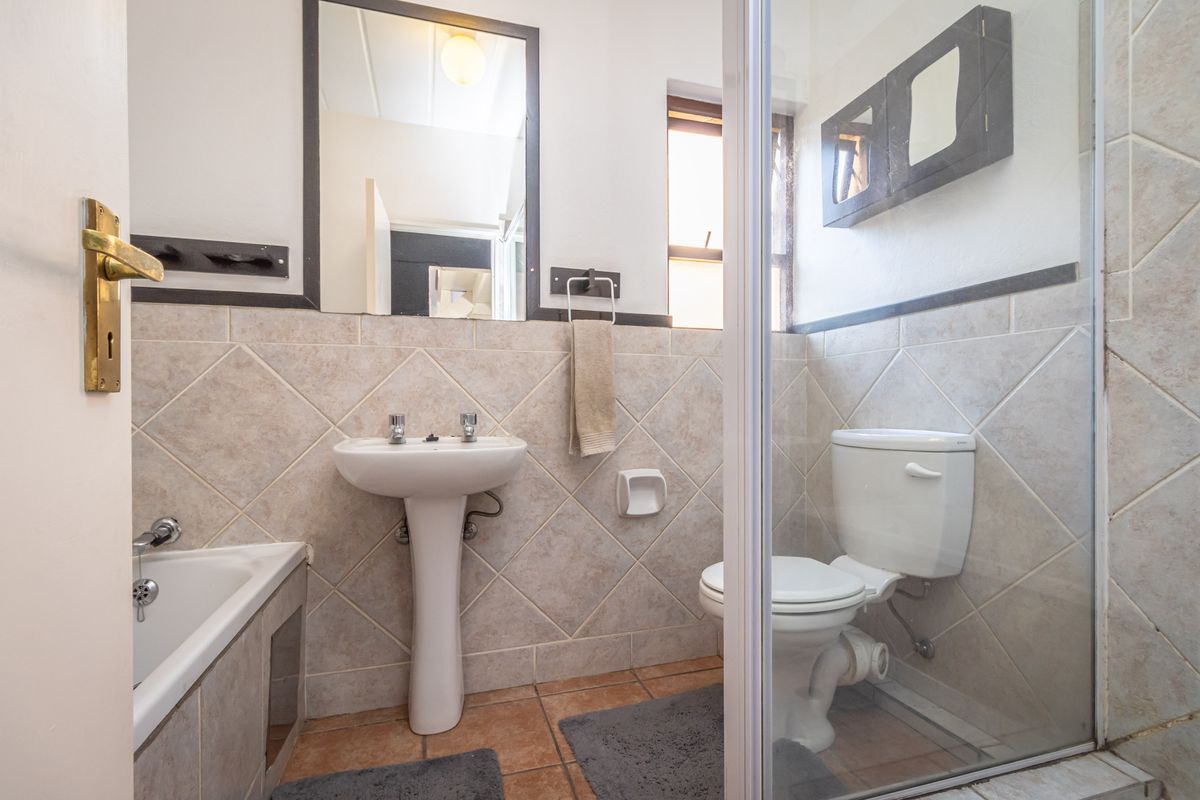 A functional bathroom featuring a pedestal basin, toilet, and a shower-over-bath combination with tiled walls and flooring.