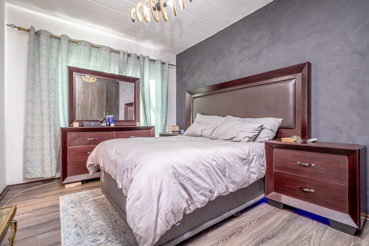 A well-proportioned bedroom featuring dark wood-look laminate flooring and a striking dark grey feature wall, providing a contemporary foundation for the space.